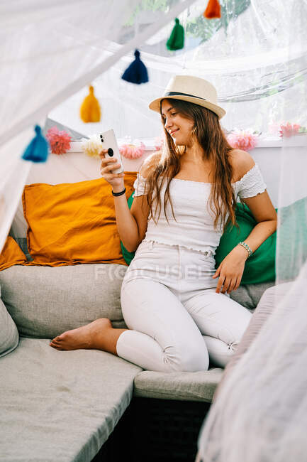 Зміст жінка сидить на дивані і обмін повідомленнями на мобільному телефоні в сонячний день у наметі на задньому дворі — стокове фото