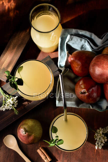 Copos de deliciosas bebidas refrescantes com suco de pêra e folhas de sabugueiro frescas na mesa com paus de canela — Fotografia de Stock