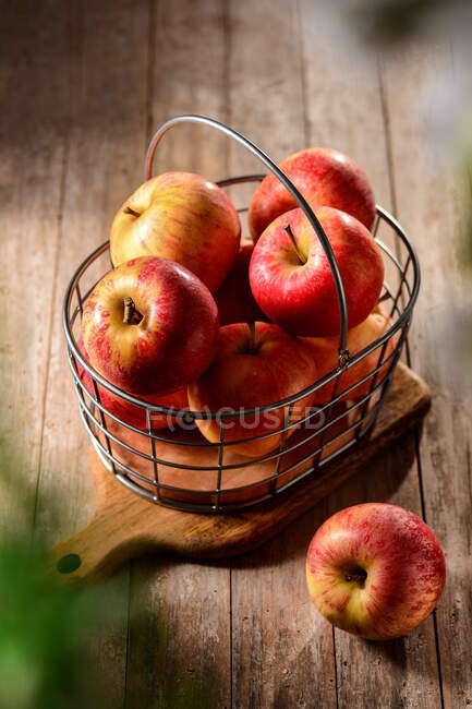 Зверху смачні стиглі яблука в металевому кошику на рубаній дошці в сільській місцевості в сонячний день — стокове фото