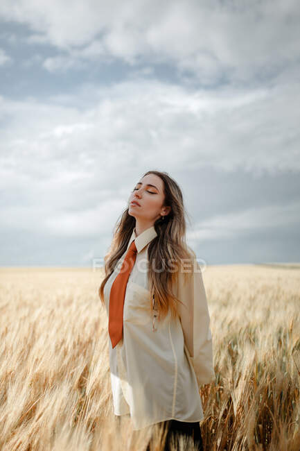 Vista lateral de la joven mujer consciente en ropa formal con corbata y ojos cerrados entre picos en el campo - foto de stock