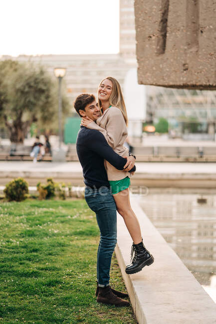 Vista lateral do namorado amoroso levantar namorada elegante na rua da cidade — Fotografia de Stock