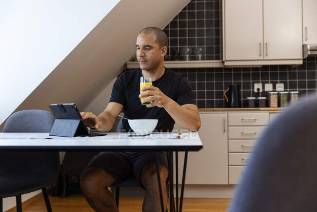 Сфокусований чоловік серфінг Інтернету на планшеті, сидячи за столом вдома і насолоджуючись сніданком вранці. — стокове фото