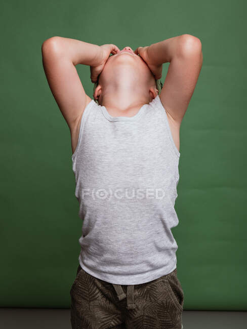 Неузнаваемый обиженный мальчик, закрывающий лицо руками и плачущий на зеленом фоне в студии — стоковое фото