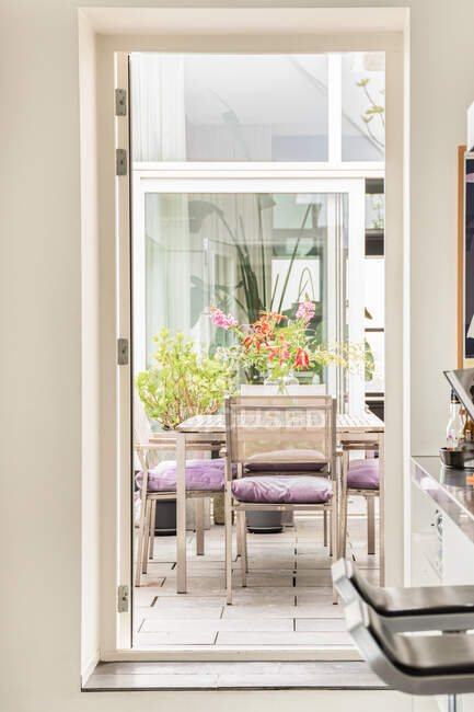 Сквозной вид на стильные стулья и стол с цветами в вазе, расположенной в обеденной зоне на террасе современного дома — стоковое фото