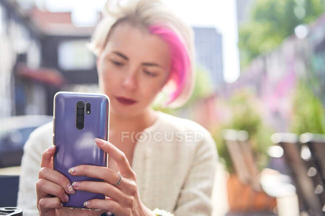 Mulher informal com cabelo curto tingido e com brilho no celular de navegação facial na cidade — Fotografia de Stock