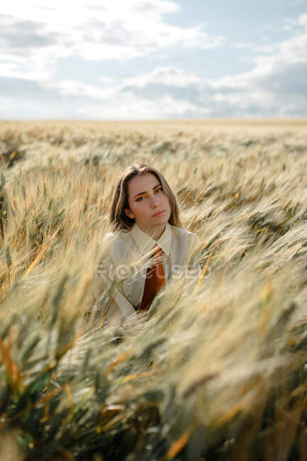 Junge Frau mit welligem Haar blickt in die Kamera auf dem Land unter wolkenverhangenem Himmel auf verschwommenem Hintergrund — Stockfoto