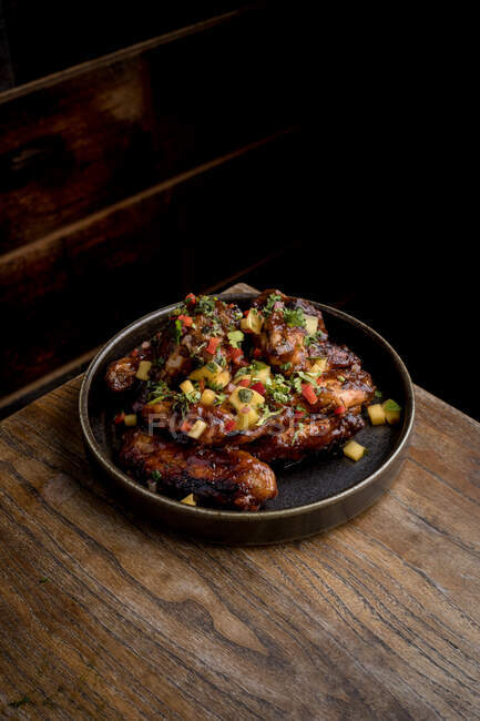 З висоти смачних курячих крил у соусі барбекю, прикрашеному свіжими овочами, подається на тарілці на дерев'яному столі в ресторані. — стокове фото