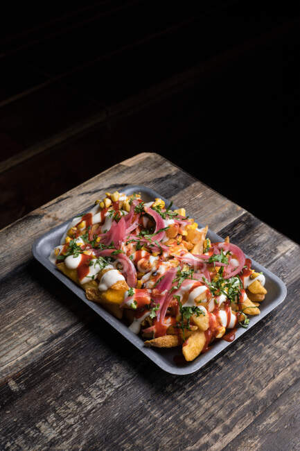Von oben Backblech mit appetitlichen Bratkartoffeln serviert mit Soßen auf Holztisch im Restaurant — Stockfoto