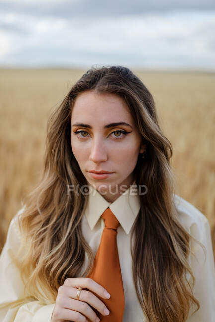 Jeune femme consciente en tenue formelle avec cravate regardant la caméra parmi les pointes dans la campagne — Photo de stock