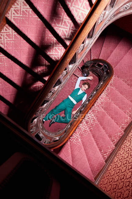 Вид сверху талантливого актера-мужчины, лежащего на полу возле лестницы и притворяющегося мертвым во время творческого представления — стоковое фото