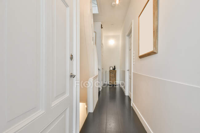Vista panorámica del pasillo estrecho y vacío con puertas y paredes blancas en apartamento moderno - foto de stock