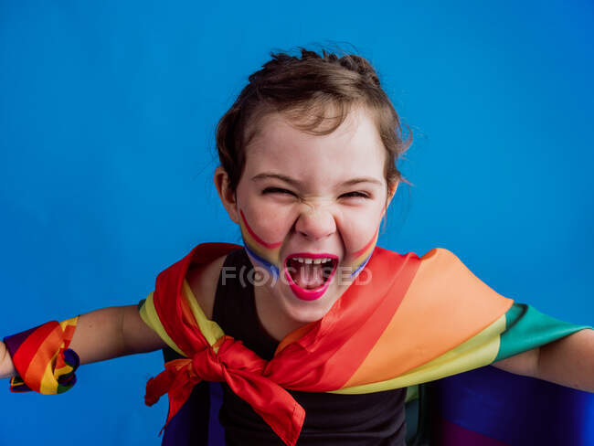 Criança feliz bonito com bandagem multicolorida no pescoço contra o fundo azul e olhando para a câmera enquanto gritos — Fotografia de Stock
