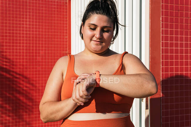 Sportswoman with curvy body checking pulse on smart watch during workout on street — Stock Photo