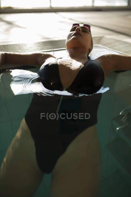Young beautiful woman lying on the curb of the indoor pool, wearing black swimsuit — Stock Photo