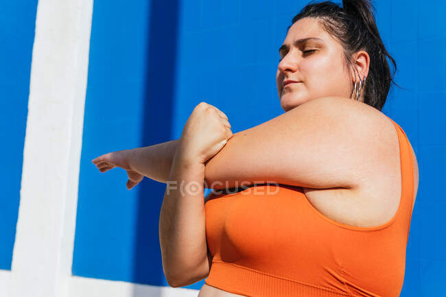 Determinato atleta donna etnica paffuto lavorando fuori mentre guardando lontano in giornata di sole su sfondo blu — Foto stock