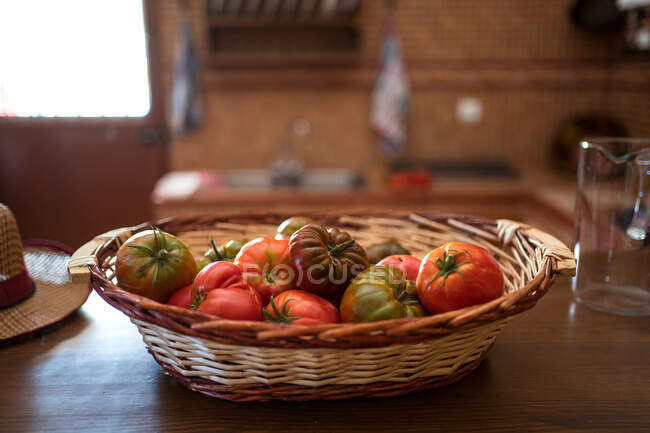 Pile de tomates fraîches dans un panier en osier placé sur la table dans la cuisine rustique pendant la saison des récoltes — Photo de stock