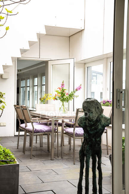 Design de interiores de luxuosa moradia com aconchegante zona de jantar decorada com flores e escultura de bronze colocada perto da porta — Fotografia de Stock