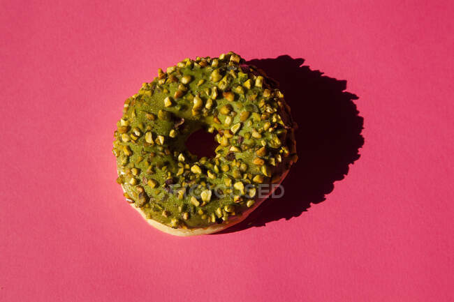 Вид зверху на один пончик, покритий зеленим цукром з горіхами на рожевому фоні — стокове фото