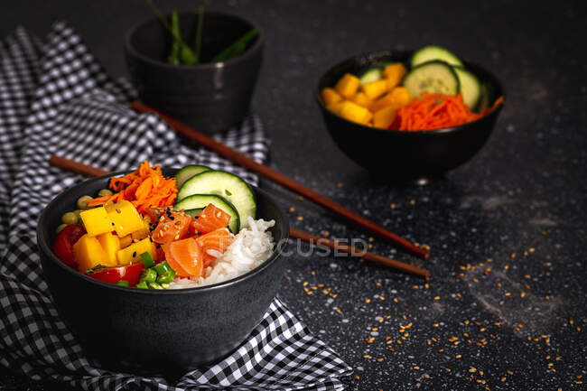 Grand angle de poke asiatique au saumon et riz avec des légumes variés servis dans un bol sur la table avec des baguettes au restaurant — Photo de stock