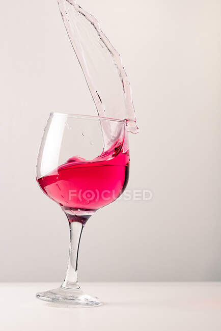 Cristallo vetro lucido con alcool cocktail spruzzi rosa su sfondo bianco in studio — Foto stock