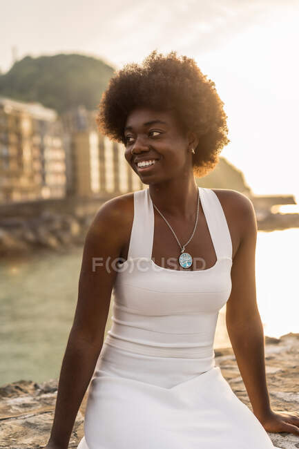 Donna afroamericana soddisfatta che si rilassa sul lungomare contro il mare la sera d'estate e distoglie lo sguardo — Foto stock