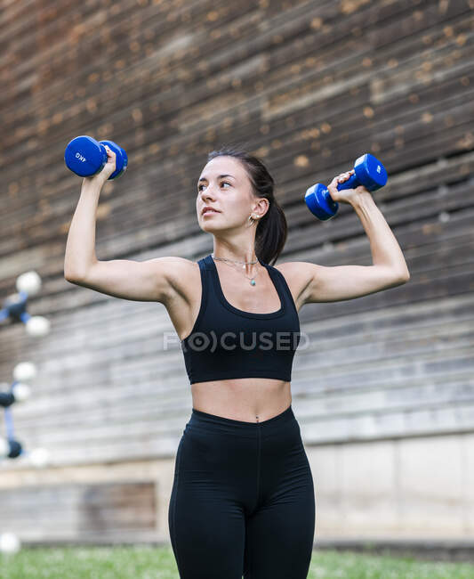 Atleta feminina determinada fazendo exercício com halteres durante o treino de fitness na rua da cidade no verão — Fotografia de Stock