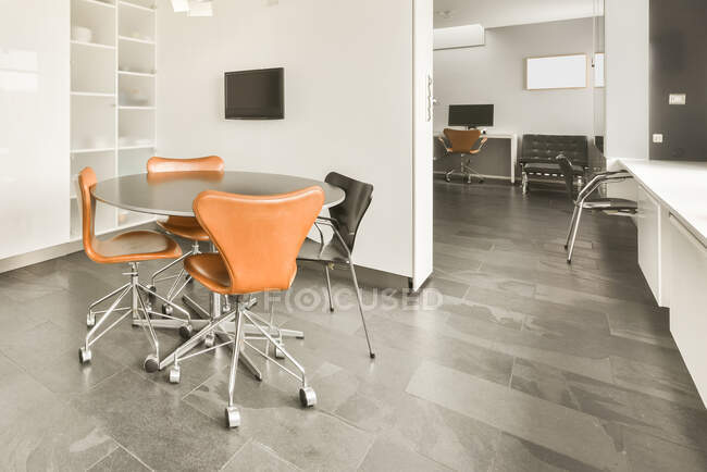 Mesa redonda e cadeiras colocadas em quarto espaçoso moderno com TV pendurada na parede branca — Fotografia de Stock