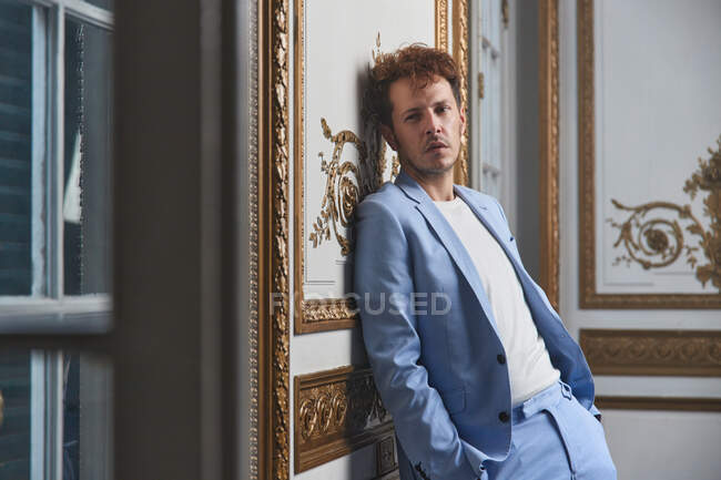 Thoughtful male in suit standing with hands in pocket and leaning on wall in posh room — Stock Photo