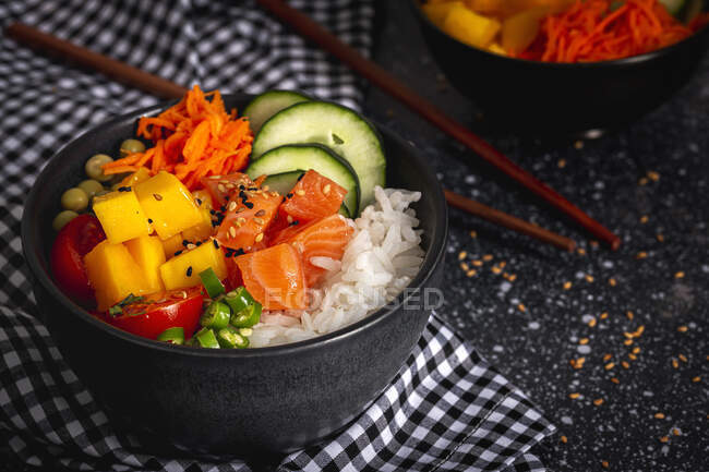 High angle of Asian poke with salmon and rice with assorted vegetables served in bowl on table with chopsticks in restaurant — Stock Photo