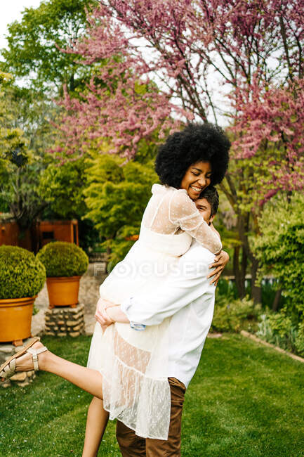 Vista laterale di uomo sollevamento donna nera mentre in piedi sul prato in giardino — Foto stock