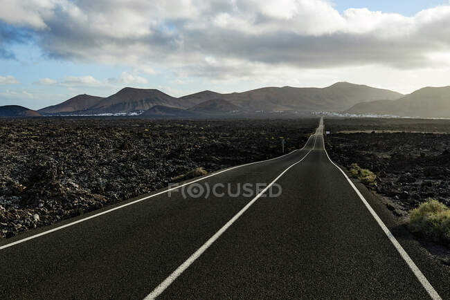 Strada asfaltata dritta che attraversa il campo verso la montagna in mattinata a Fuerteventura, Spagna — Foto stock