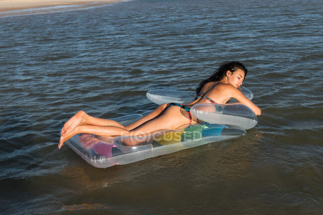 Contenido hembra acostada en colchón inflable flotando en el agua de mar en día soleado en verano y ojos cerrados - foto de stock