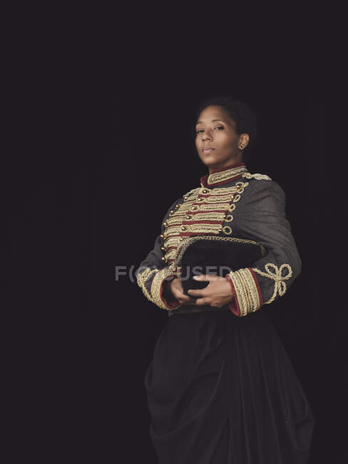 Fiduciosa donna afroamericana adulta in elegante giacca guardando la fotocamera in studio scuro su sfondo nero — Foto stock
