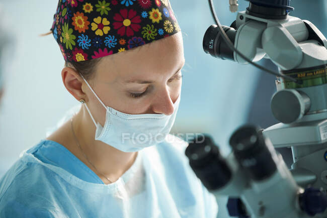 Adulto médico feminino em uniforme cirúrgico e máscara estéril sentado na clínica — Fotografia de Stock