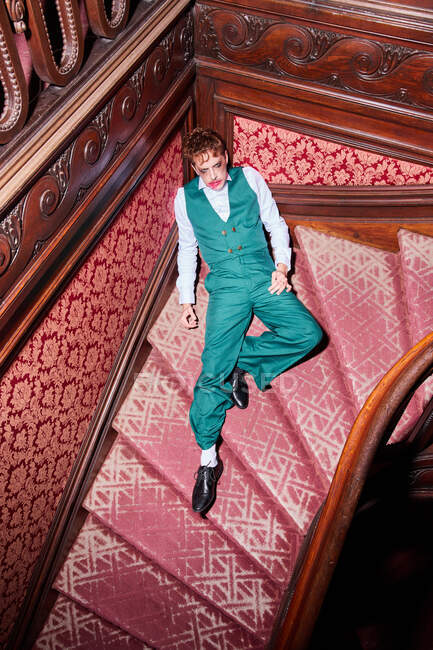 Desde arriba de actor masculino excéntrico con maquillaje untado sentado en la escalera durante la actuación - foto de stock