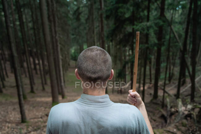Rückansicht eines nicht wiedererkennbaren Mannes mit Stock, der auf einem Felsen in der Nähe von Bäumen steht, während er Kung Fu im Nadelwald übt — Stockfoto
