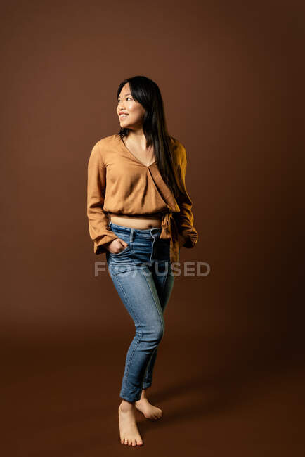 Front view of Asian female in trendy clothes looking away on brown background in studio — Stock Photo