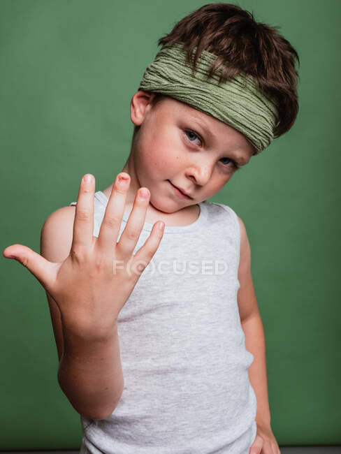 Alegre menino karatê pré-adolescente em lenço hachimaki e com a mão olhando para a câmera em fundo verde no estúdio e se divertindo — Fotografia de Stock