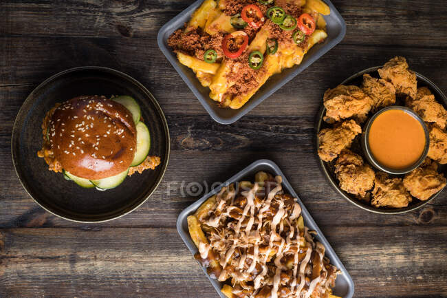 Hoher Tisch mit leckeren Pommes frites mit Büffelkäse in der Nähe von Chicken Burger und knusprigem Huhn mit Sauce im Restaurant — Stockfoto