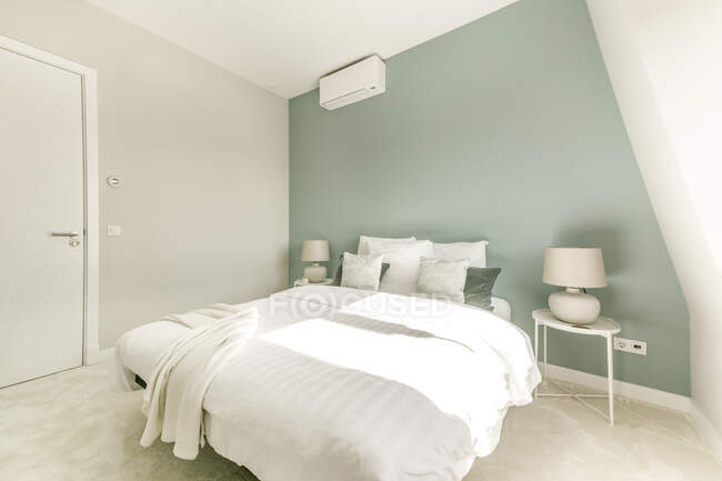 Interior de dormitorio contemporáneo con cama con almohadas suaves colocadas cerca de la ventana en el apartamento en estilo minimalista - foto de stock