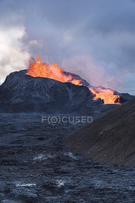 Живописный вид на Fagradalsfjall с быстрым огнем и лаву под рассеивающимся дымом в горах с пушистыми облаками в Исландии — стоковое фото