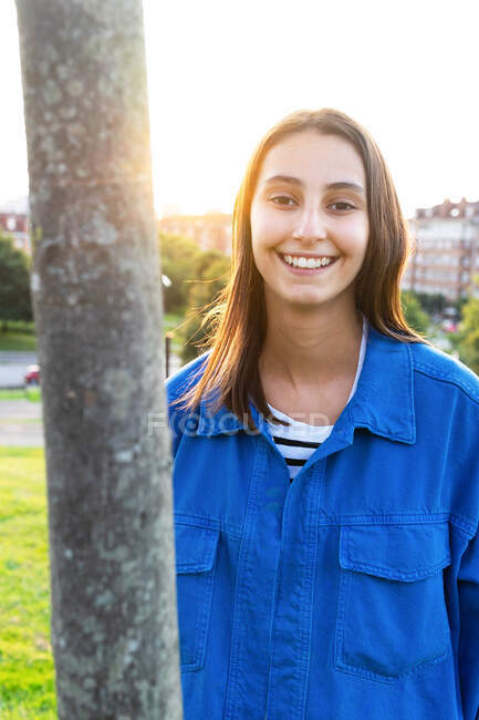 Fröhliche Frau mit Brille guckt aus Baumstamm im Stadtpark und blickt in Kamera — Stockfoto
