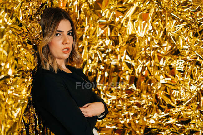 Young gentle female with makeup looking at camera against creased golden foil — Stock Photo