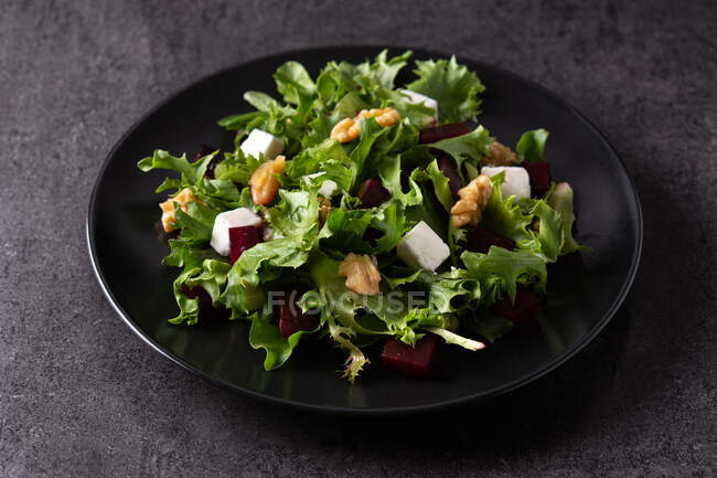 Hoher Winkel des schwarzen Tellers mit leckerem Rote-Bete-Salat mit Tofu-Käse und grünem Salat, serviert auf dunklem Hintergrund im Studio — Stockfoto