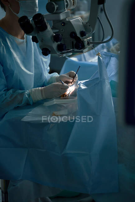 Crop anonymous eye surgeon with manual instruments operating patient on medical bed in hospital on blurred background — Stock Photo