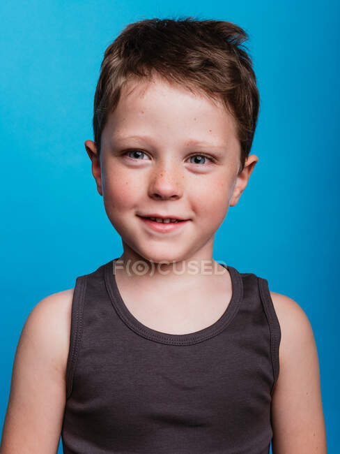 Contenido adorable niño preadolescente mirando a la cámara en el fondo azul brillante en el estudio - foto de stock