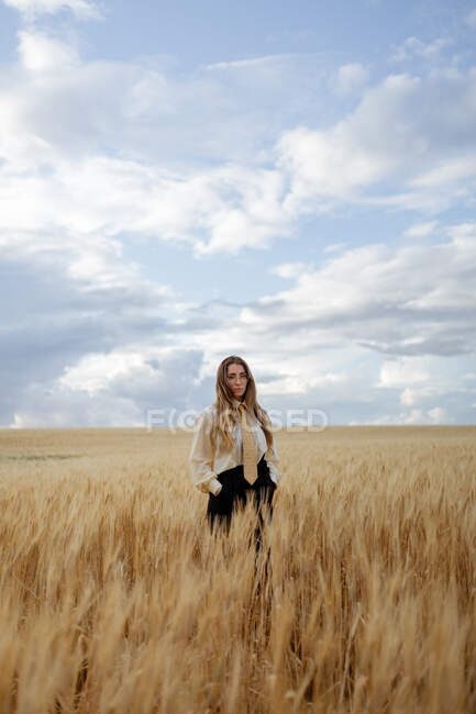 Young mindful female in glasses and in formal wear with tie looking at camera among spikes in countryside — Stock Photo