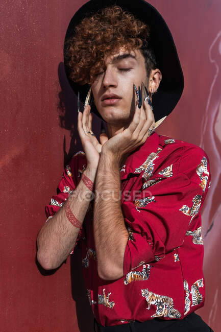 Dreamy young feminine gay with closed eyes and tattoo in stylish apparel touching face in sunlight — Stock Photo