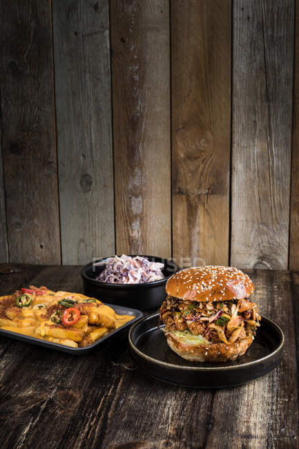 Antipasto hamburger con carne alla griglia posto vicino alla teglia con patatine al formaggio con peperoni e ciotola con insalata sul tavolo di legno nel ristorante — Foto stock