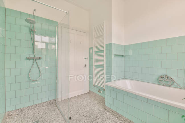 Interior design of spacious light bathroom with window and green tiles on walls furnished with bathtub and washbasin and decorated with potted plants at home — Stock Photo